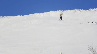 Freeride snowboard kar toz mavi gökyüzüne karşı geride bırakarak bir karla kaplı yamaç rulo. Video. Snowboard dağdan aşağı rulo