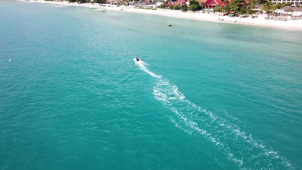 Aerial view of white sand beach and jet ski on the blue lagoon aqua sea. Aerial birds eye view of jet ski cruising in high speed in turquoise clear water sea