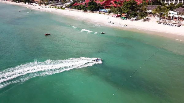 Aerial view of white sand beach and jet ski on the blue lagoon aqua sea. Aerial birds eye view of jet ski cruising in high speed in turquoise clear water sea