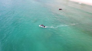Beyaz kumlu sahil manzarası ve mavi göl sularında jet ski. Açık deniz turkuazında yüksek hızda uçan jet ski 'nin havadaki kuş bakışı görüntüsü..