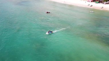 Beyaz kumlu sahil manzarası ve mavi göl sularında jet ski. Açık deniz turkuazında yüksek hızda uçan jet ski 'nin havadaki kuş bakışı görüntüsü..