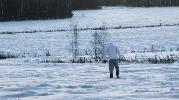 Una persona en un campo cubierto de nieve. Filmación. Vista trasera del hombre caminando en el campo nevado profundo. Hombre caminando en la nieve vista trasera — Foto de Stock