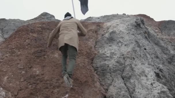Mannen med flaggan på toppen av berget infogar en flagga i marken, underifrån på nära håll. Footage. Vandrare i berget. bergklättrare på toppen. Bergsklättring — Stockvideo