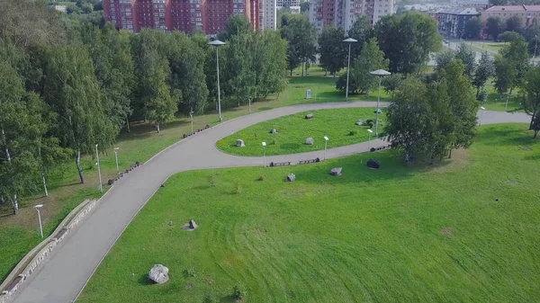 Зеленый парк и его огромные лужайки в солнечный весенний день. Клип. Воздушный беспилотник городского парка с пешеходной дорожкой и зелеными деревьями. Велосипедист в парке — стоковое фото