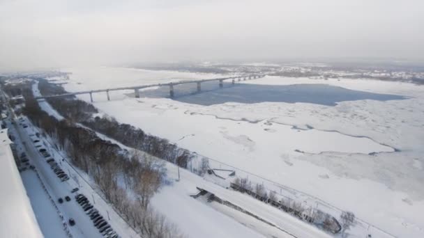 Hiver enneigé dans la belle ville ou la ville. Clip. Vue de dessus de la rivière gelée, de nombreuses voitures sur la route, bâtiments anciens. Charmante période hivernale dans la grande ville. Magnifique panorama 