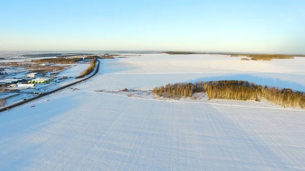 A winter field with a dawn and an orange sun in the sky with clouds. Aerial drone view of winter snowy countryside at sunset. Aerial drone view of winter snowy countryside. Village in the forest