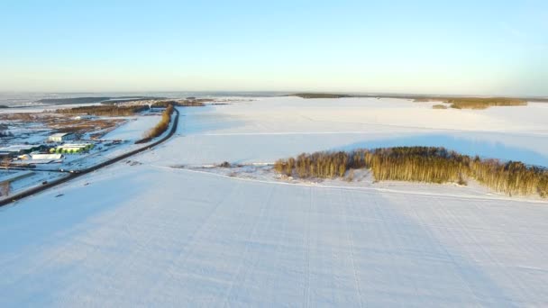Um campo de inverno com um amanhecer e um sol laranja no céu com nuvens. Vista aérea do drone da paisagem nevada do inverno no por do sol. Vista aérea drone de inverno campo nevado. Vila na floresta — Vídeo de Stock