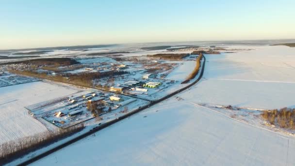 Landsbygdens vinterlandskap. Flygfoto. Flygfoto över små byn vintertid. Flygfoto över vintern snöiga landskapet vid solnedgången. Fält som är täckt med snö och skog — Stockvideo