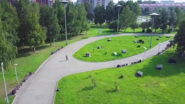 Weg in de buurt van het groene park, bovenaanzicht. Green Park en haar grote gazons op een zonnige lentedag. Clip. Luchtfoto van het gedreun van een stadspark met wandelen pad en groene zone bomen vliegen. Fietser in het Park — Stockvideo