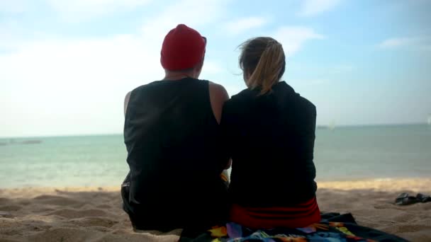 Vista traseira do casal sentado na areia junto ao mar e de volta natureza do verão. Vídeo. Feliz casal amoroso em um penhasco vista tropical belo mar cristalino na ilha tropical — Vídeo de Stock