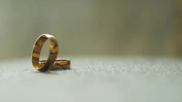 Egy arany Karikagyűrű hengerelt a másikra. Videó. Esküvő gyűrű. Két jól használható Arany eljegyzési gyürük, szürke háttér. Közeli kép: menyasszonyi ékszer, a házasság. — Stock Fotó