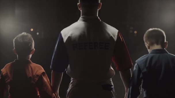 Rear view of the boys athletes and referee who raises the hand of the winner. The referee raises the hand of the boy winner in the ring. Judo — Stock Video