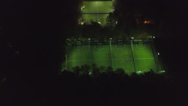 Aerial view of football pitch at night with amateur football players playing the game in the city. Clip. Football soccer field night aerial — Stock Video