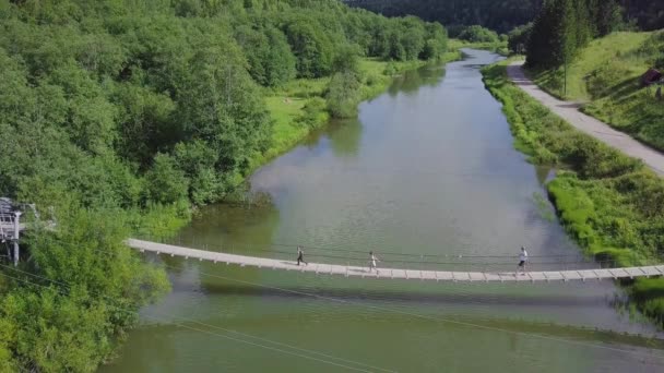 Unidenfied mensen lopen over de lange metalen hangbrug over de rivier. Clip. Familie op de brug over de rivier — Stockvideo