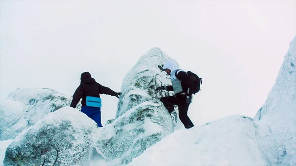 Jovens homens montanhosos escalando no pico nevado. Vídeo. Dois alpinistas em pé no topo do cume acima das nuvens nas montanhas. Dois alpinistas sentados no cume da montanha — Fotografia de Stock