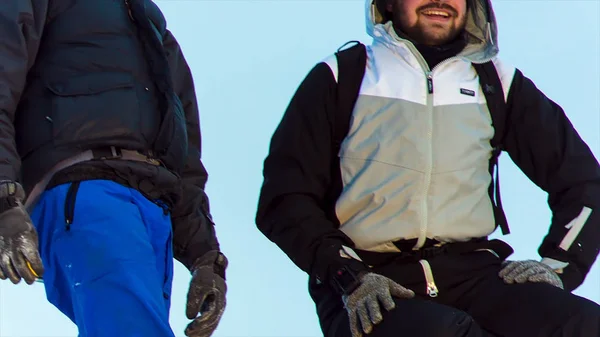 Jovens homens montanhosos escalando no pico nevado. Vídeo. Dois alpinistas em pé no topo do cume acima das nuvens nas montanhas. Dois alpinistas sentados no cume da montanha — Fotografia de Stock
