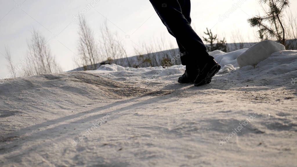 Close-up of male legs in winter shoes walking on snow. View of walking on snow with Snow shoes and Shoe spikes in winter. Mens legs in boots close up the snow-covered path