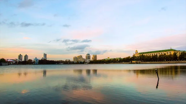 Scenic panorama cityscape, city reflected on lake at sunset. Video. Urban night scene. Panorama of city shore of lake with buildings background and sunset — Stock Photo, Image