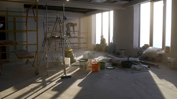 Silhouette de deux constructeurs et réflexion du soleil et de la lumière à travers la fenêtre. Travailleur de la construction avec casque dur travaillant sur le site, rénovation de la maison. équipe de constructeurs finisseurs travaillent à l'intérieur — Photo