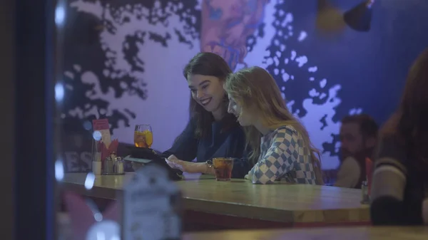 İki kadın arkadaş tablet bilgisayar kafe, açık havada oturma grubu. Güzel kız arkadaşları ile smartphone ve tablet kafede. Bir tablet Pc ve gülmek kafede oturan iki güzel kız arıyorum. — Stok fotoğraf
