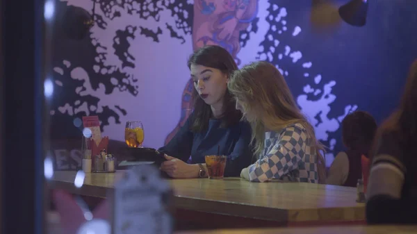 Dwie piękne kobiety młody siedząc w kawiarni i patrząc cyfrowych tabletu. Praca zespołowa, dwóch młodych przedsiębiorców, siedząc przy stoliku w kawiarni. Atrakcyjną kobietę i jej przyjaciel przytrzymaj tabletkę — Zdjęcie stockowe