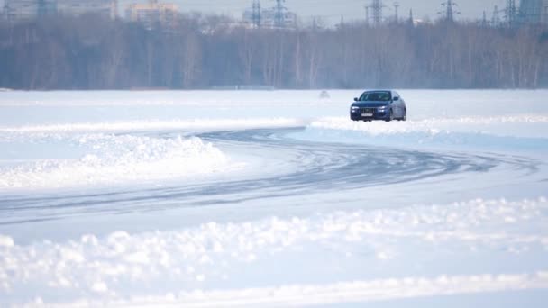Conducción de invierno. Coche azul conduce por pista helada en el lago cubierto de nieve en invierno. Carreras de coches deportivos en pista de carreras de nieve en invierno. Conducir un coche de carreras en una carretera nevada — Vídeo de stock