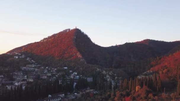 Luchtfoto - landschap van boom, berg vanaf de top van de berg op zonsondergang tijd. Clip. Bovenaanzicht van de berg stad bij zonsondergang — Stockvideo