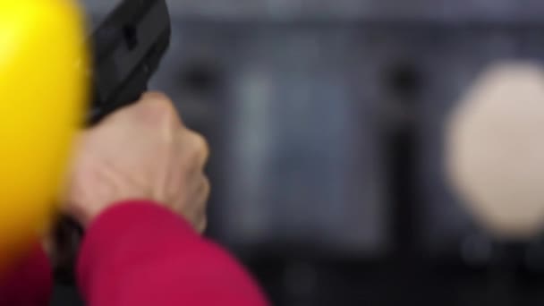 Pohled muž střílí zbraň na střelnici zblízka zezadu. Člověk je vyvoláno ruční pistole na kryté střelnici. Zblízka. Detailní záběr z mužských rukou s pistolí, muž vlaky střílet zadní pohled — Stock video