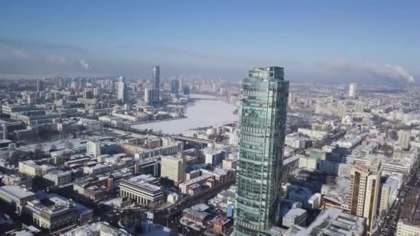 Ovanifrån av fantastiska glas tornet eller businesscenter i bakgrunden av en Vinterstaden. Flygfoto över skyskrapa är mitt i city i vinter, Himmelsblå sky och snöiga tak av — Stockvideo