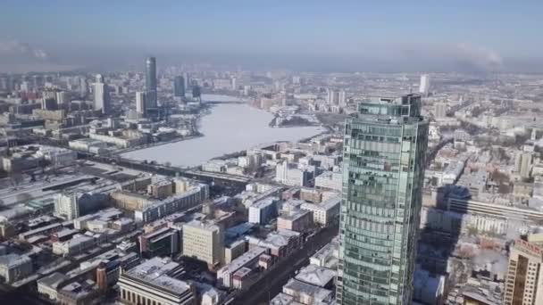 Top view of the amazing glass tower or the business center in the background of a winter city. Aerial view of skyscraper is in the middle of the city in winter, blue sky sky and snowy roofs of — Stock Video