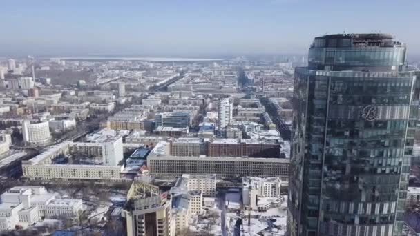 Вид зверху на дивовижну скляну вежу або бізнес-центр на тлі зимового міста. Вид з повітря на хмарочос посеред міста взимку, блакитне небо і снігові дахи — стокове відео