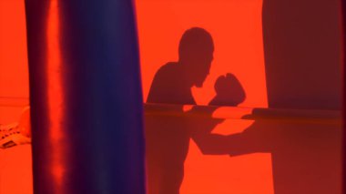 Siluet veya kum torbasına yakın kadar kırmızı ışık arka plan Delme bir boksör gölgesi. Kum torbası kırmızı zemin üzerine isabet genç erkek boxer silüeti. Adam atlet ayakta ve boks.