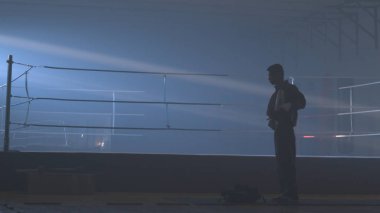 Savaşçı adam siluet karanlık. MMA savaşçı siluet karanlık halkası üzerinde. Boksör mücadele önce sahnede duruyor. Boksör siluet duman karanlık stüdyoda. Arkadan görünüş adam boks halka yakın Tarih