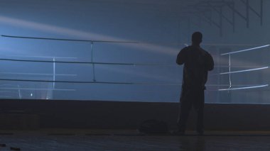 Savaşçı adam siluet karanlık. MMA savaşçı siluet karanlık halkası üzerinde. Boksör mücadele önce sahnede duruyor. Boksör siluet duman karanlık stüdyoda. Arkadan görünüş adam boks halka yakın Tarih
