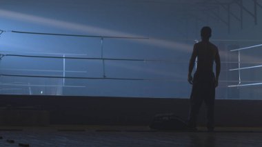 Grunge arka plan üzerinde arkadan görünüm genç boksör. Savaşçı adam siluet karanlık. MMA savaşçı siluet karanlık halkası üzerinde. Boksör mücadele önce sahnede duruyor. Boksör siluet duman karanlık stüdyoda. Arkadan görünüş
