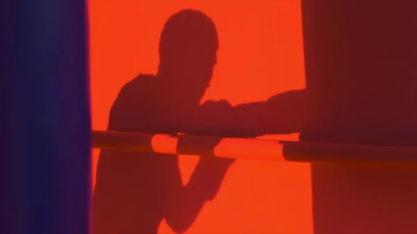 Silhouette or shadow of a boxer punching a punching bag close up, red light background. Silhouette of young male boxer hitting punching bag on red background. Man athlete standing and boxing.