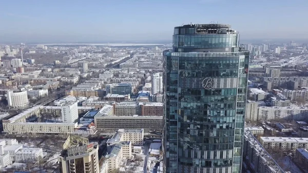 Blick von oben auf den wunderschönen Glasturm oder das Business Center im Hintergrund einer Winterstadt. Luftaufnahme des Wolkenkratzers liegt mitten in der Stadt im Winter, blauer Himmel und schneebedeckte Dächer von — Stockfoto