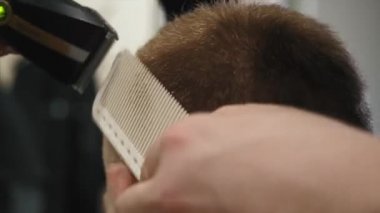 Yakın çekim konsantre kahverengi saçlı işadamı onun saç taranmış ve bir kuaför dükkanı kesilmiş olması. Küçük. Kuaför müşteri makine ile keser.