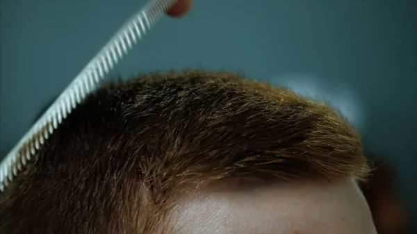 Primer plano de un empresario de cabello castaño concentrado peinándose y recortándose el pelo en una peluquería. Clip. Peluquero corta a un cliente con máquina —  Fotos de Stock