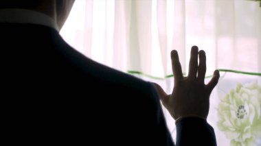 Üzerinde bir ceketli adamı arkadan görünüm penceresi, elini kaldırdı duruyor. Küçük. Bir pencere önünde duran ve dışarı bir yatak odasında evde arayan bir insanın arkadan görünüş