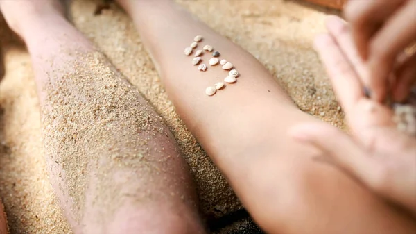 As mãos femininas reúnem o modelo de conchas e areia, perto. Vídeo. Pedaços de âmbar e conchas em mãos femininas em um fundo de areia. Menina brinca com conchas e areia sentada na praia . — Fotografia de Stock