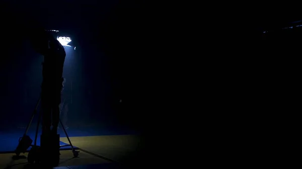 The film crew works on creation of a videoclip. Gaffer prepares diffusion for a light in the studio. Gaffer puts blue gel on a fresnel light on video production set