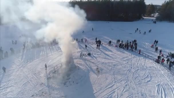 Muitas pessoas olham a queimadura do manequim durante a celebração de férias tradicionais russas Maslenitsa à tarde de inverno. Filmagem. Vista aérea — Vídeo de Stock