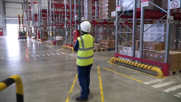 Tiro de trabalhador industrial feminino no chapéu duro andando através da indústria pesada Manufacturing Factory. Clipe. Visão traseira do trabalhador armazém feminino vestindo óculos de proteção e capacete — Fotografia de Stock