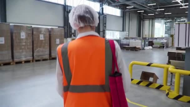 Volg beelden van fabrieksarbeider in een helm die door middel van industriële voorzieningen loopt. Clip. Volgende schot van industriële werkneemster in de harde hoed wandelen door zware industrie — Stockvideo