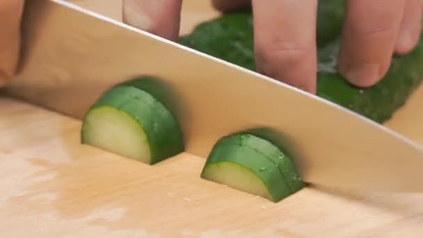 Close-up van handen van chef-kok snijden van een komkommer met een stalen mes op een snijplank. Clip. Chef-kok snijden een groene komkommer in de keuken — Stockvideo