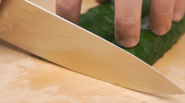 Primer plano de las manos del chef cortando un pepino con un cuchillo de acero en una tabla de cortar. Clip. Chef cortando un pepino verde en la cocina — Foto de Stock