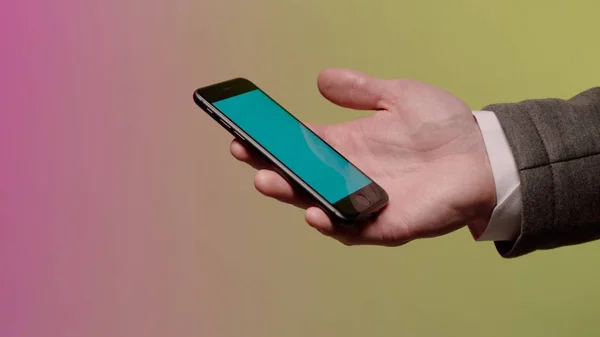 The hand of a businessman who keeps a smart-phone. Stock. Sleeve jacket and shirt parts. Green screen. Click on the screen of the mobile phone
