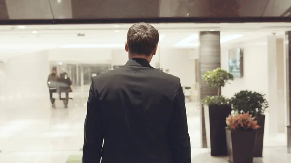 Rear view of businessman near the reception. Stock. There are glass wall offices. Rear view of businessman in hotel