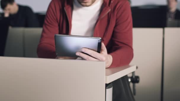 Un jeune étudiant assis au bureau interagit avec une tablette et lit des livres. Des actions. L'éducation. Université — Video